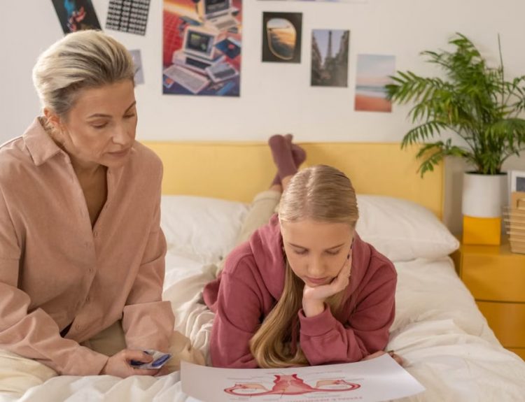 A mother and daughter talk over illustrated materials in a cozy bedroom setting.