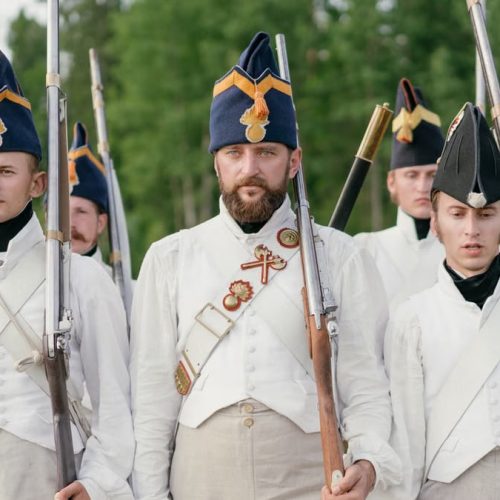 Soldiers marching in historical military uniforms reenact past events outdoors.