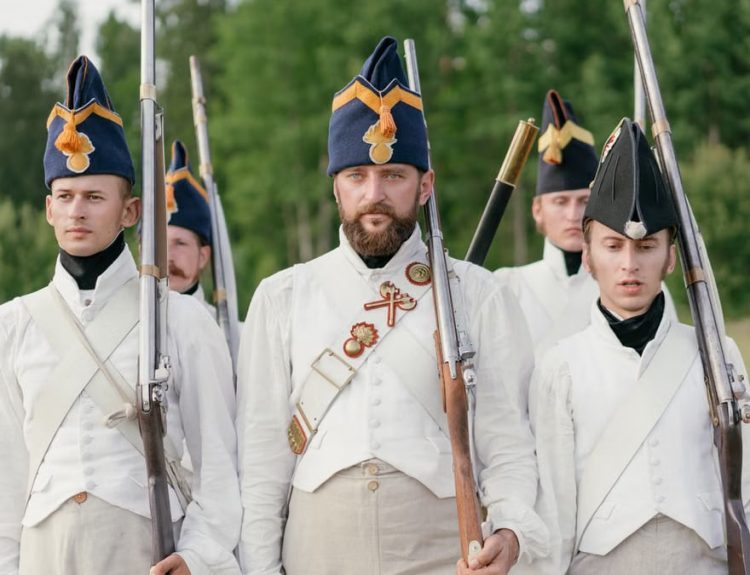 Soldiers marching in historical military uniforms reenact past events outdoors.